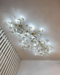 Long ceramic ginkgo flush mount ceiling light installed beside a white slatted wall in a cool camera exposure.