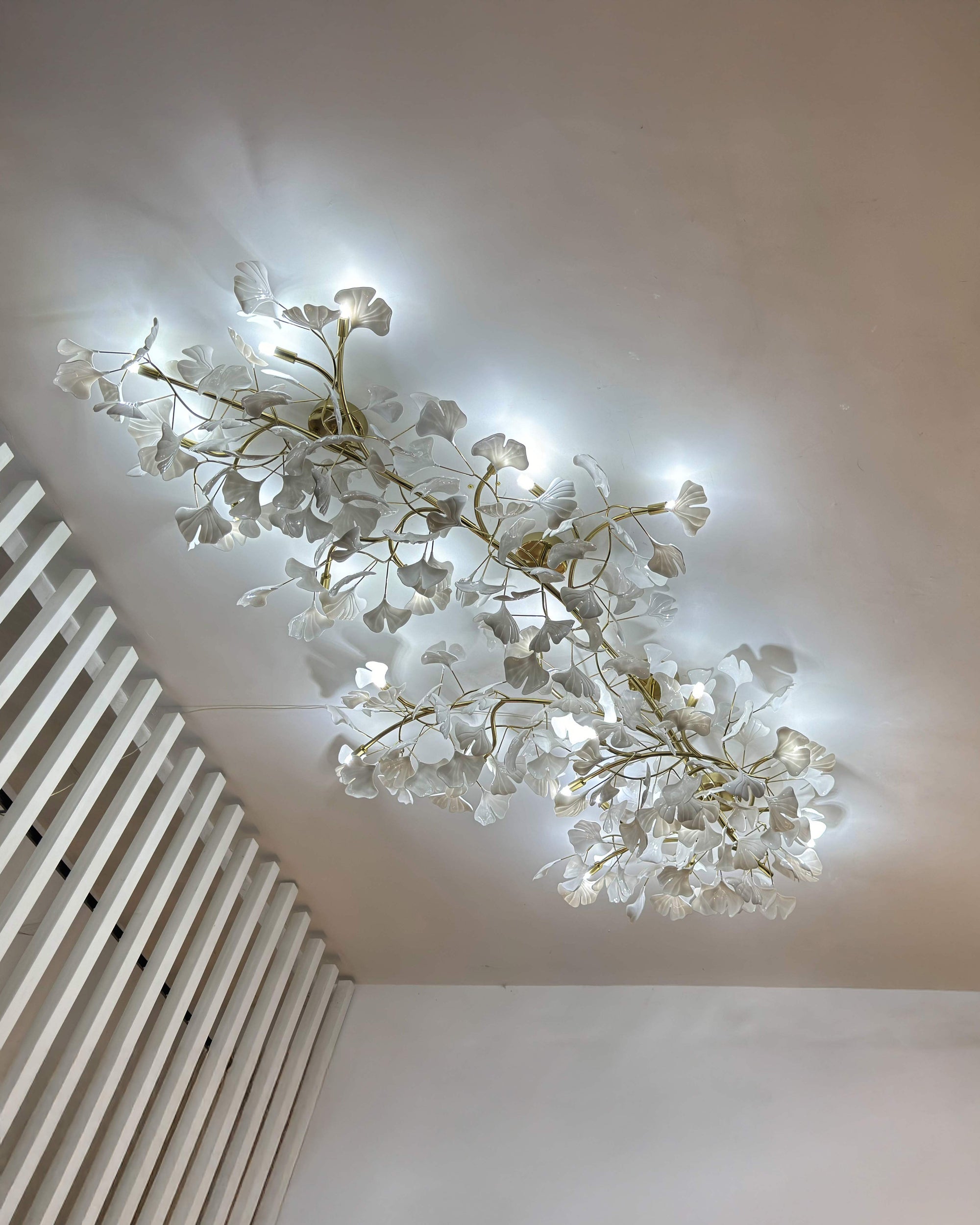 Long ceramic ginkgo flush mount ceiling light installed beside a white slatted wall in a cool camera exposure.