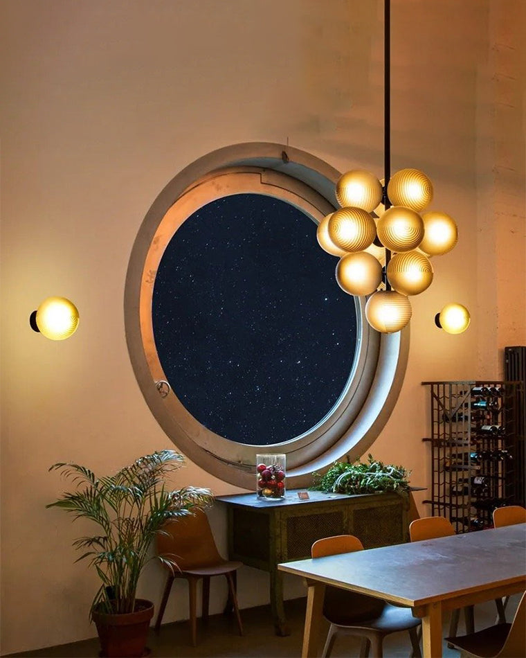 Warm-lit grape chandelier suspended beside a round mirror in a stylish dining area.