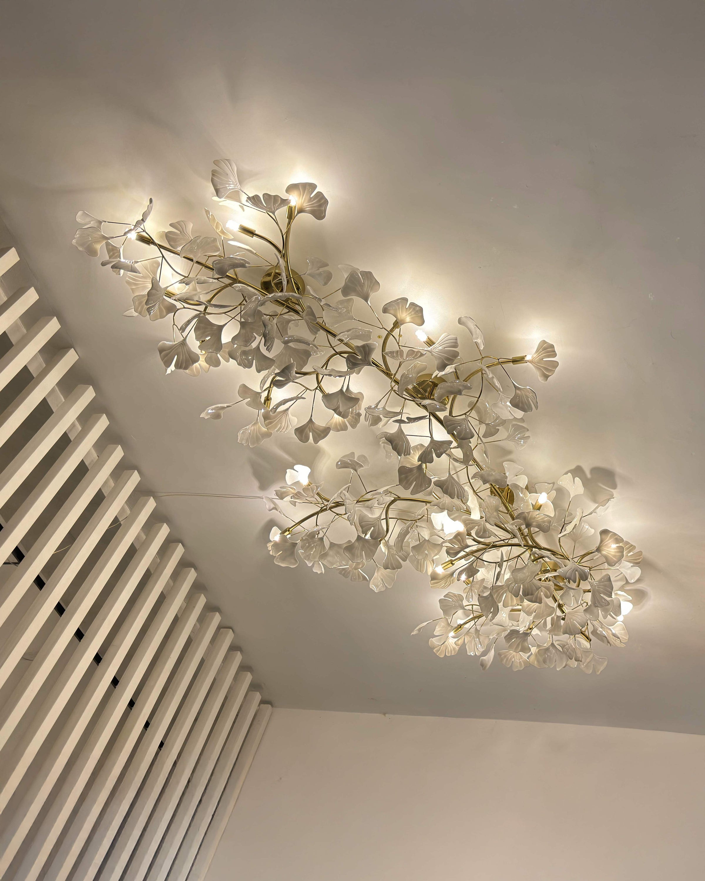 Warm-white view of the long ceramic ginkgo ceiling light with layered white leaves and curved gold branches.