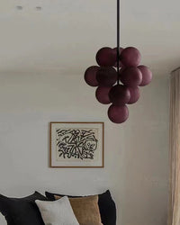 Unlit purple grape chandelier hanging above a bed in a neutral bedroom.