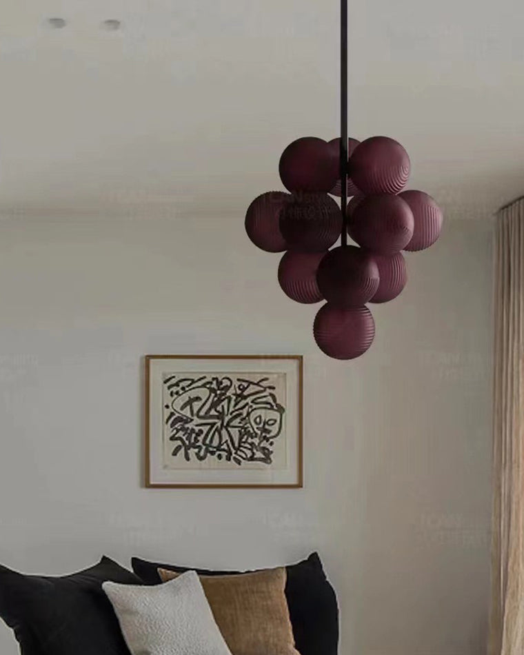 Unlit purple grape chandelier hanging above a bed in a neutral bedroom.