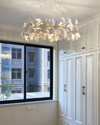 Round ceramic leaf chandelier installed beside a window and white paneled storage cabinets.