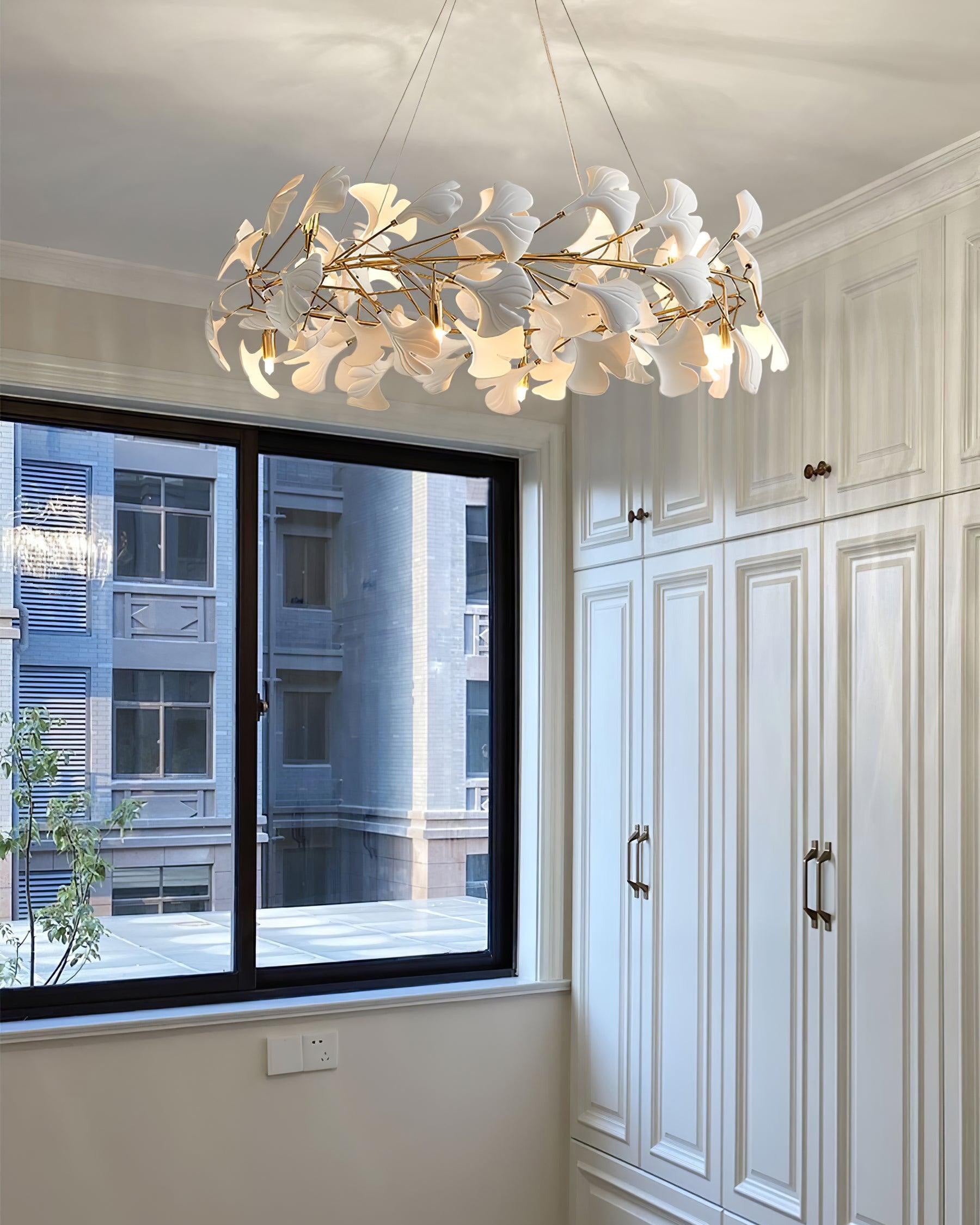 Round ceramic leaf chandelier installed beside a window and white paneled storage cabinets.
