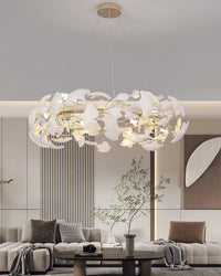White modern chandelier glowing above a minimalist sectional, with layered ceramic leaves bringing soft botanical texture to the room.