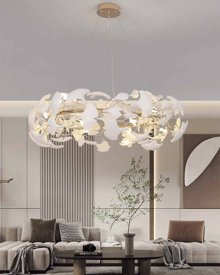 White modern chandelier glowing above a minimalist sectional, with layered ceramic leaves bringing soft botanical texture to the room.