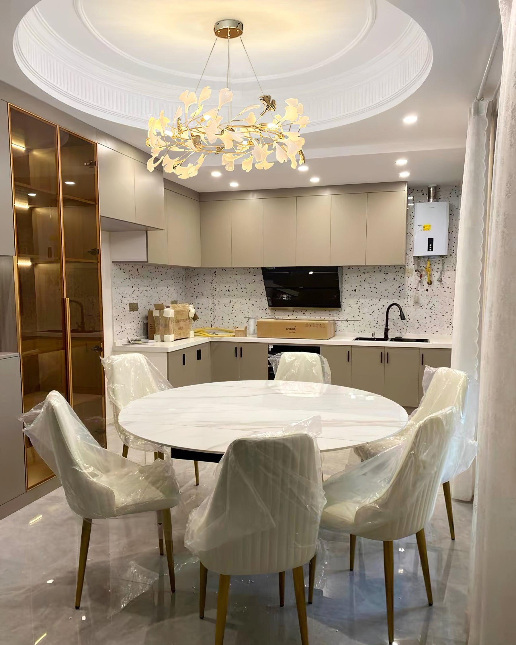 Gold round chandelier above a white circular dining table beside a compact kitchen.