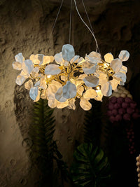 Warm light glowing between layered white ceramic blooms and reflective brass branches against a textured wall.
