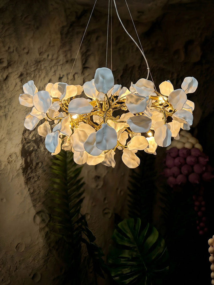 Warm light glowing between layered white ceramic blooms and reflective brass branches against a textured wall.