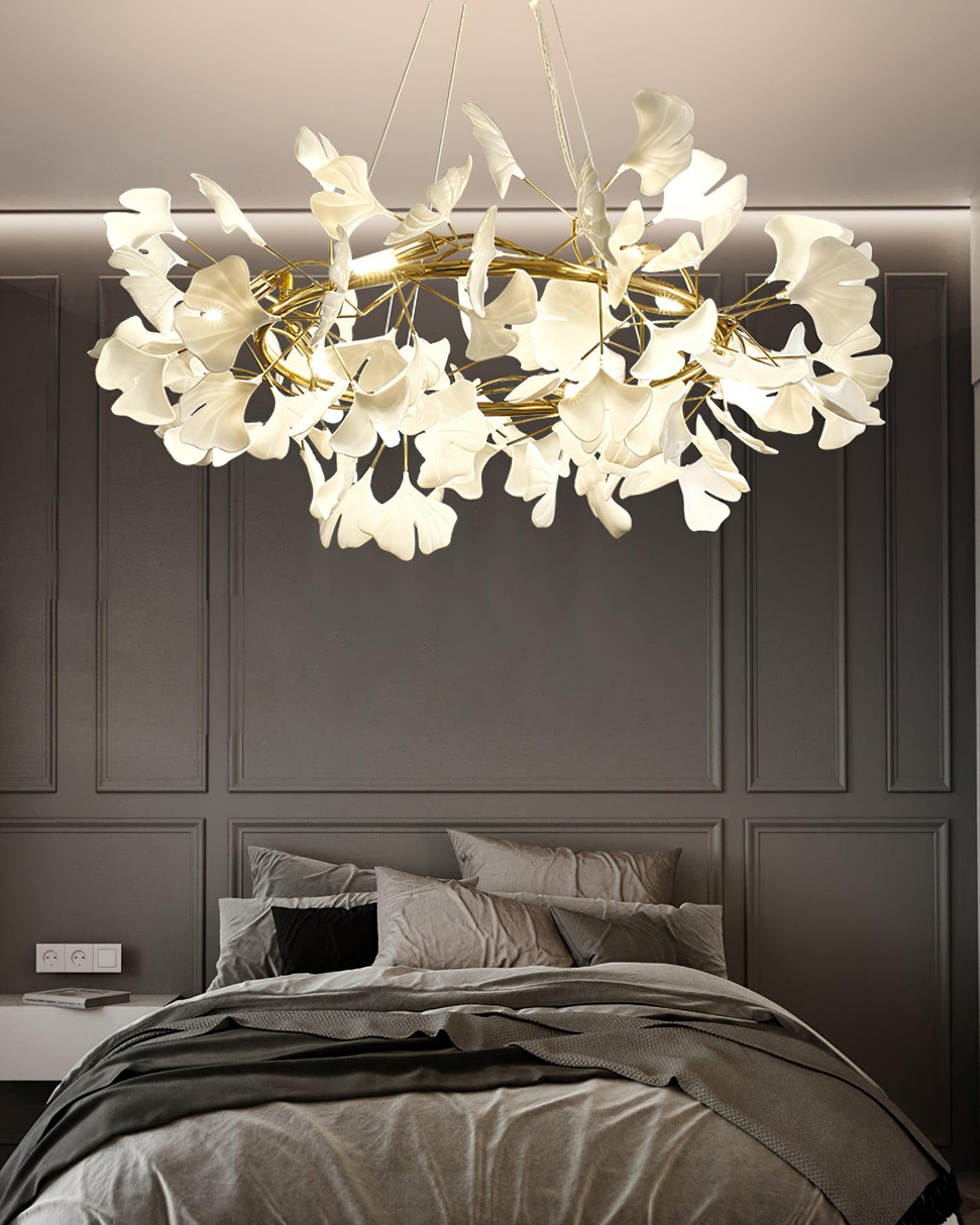 Gold-framed ceramic leaf chandelier above a dark upholstered bed in a modern bedroom.