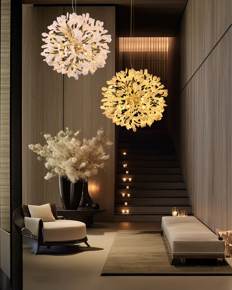 A stylish entry hall with wooden accents and a staircase, featuring two floral globe chandeliers (one white, one gold) suspended from the ceiling casting warm light.