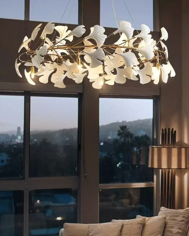 Close view of the WM2419 ginkgo leaf chandelier glowing at dusk beside large windows, highlighting warm light and layered white leaves.