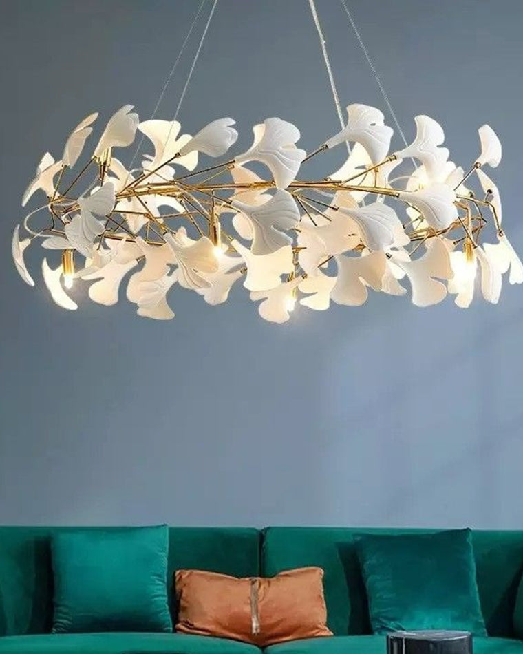 White leaf chandelier glowing above an emerald sofa, shown close enough to reveal the warm bulbs and layered ceramic leaf silhouette.