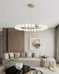 A luminous pearl ring brightens the wood-toned living room, balancing a clean circular profile with restrained gold detailing and an airy suspended form.