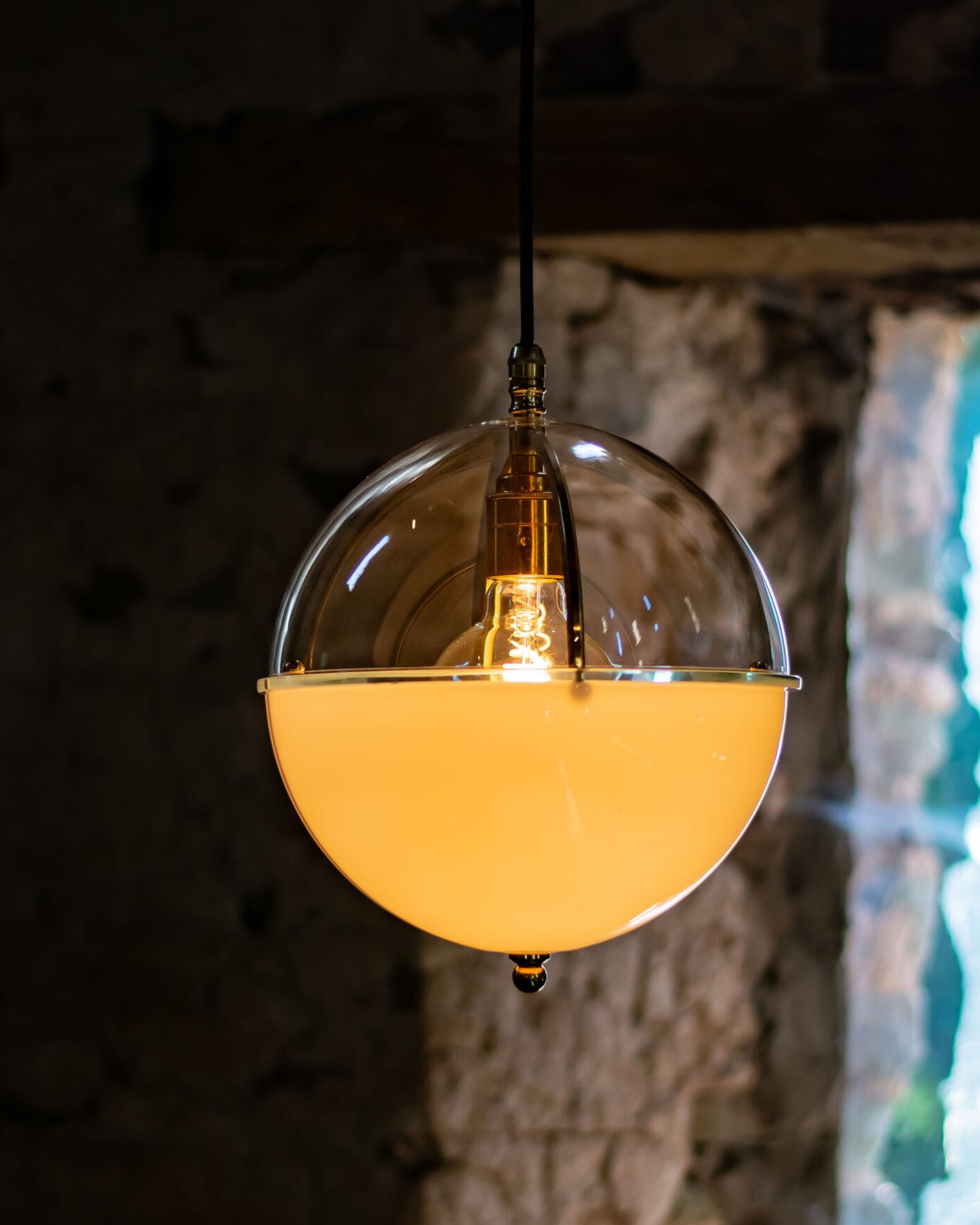 Clear-and-white glass globe hanging light glowing warmly against a textured interior wall.