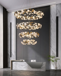 Four-tier ginkgo chandelier glowing above a tall marble reception foyer with white leaves and gold reflections.