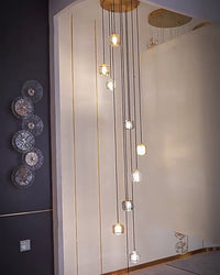 Long-drop foyer chandelier with slender glowing pendants, designed to fill vertical space beside statement wall art in an entryway.