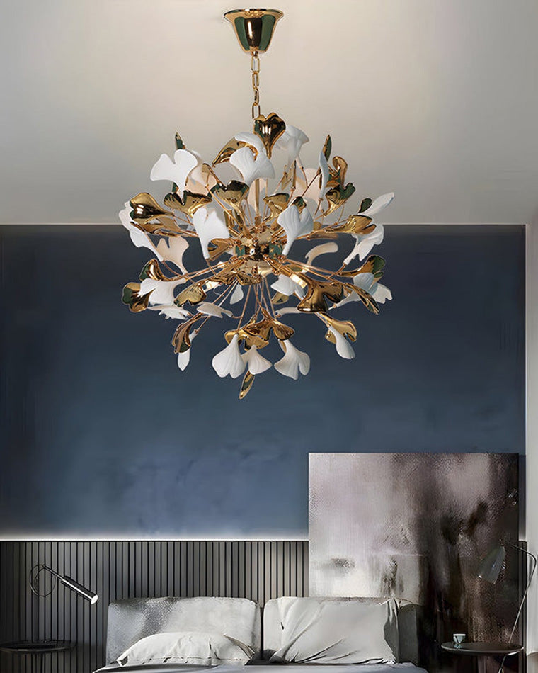 Close-up of a bedroom with a gray upholstered bed and dark walls; a luxurious white and gold ginkgo leaf chandelier hangs from the ceiling above.