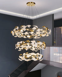Modern staircase chandelier filling a tall stairwell with three illuminated rings of white ginkgo leaves.