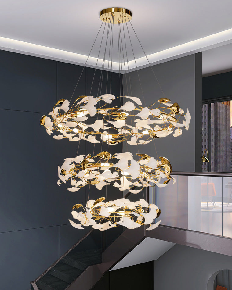 Modern staircase chandelier filling a tall stairwell with three illuminated rings of white ginkgo leaves.