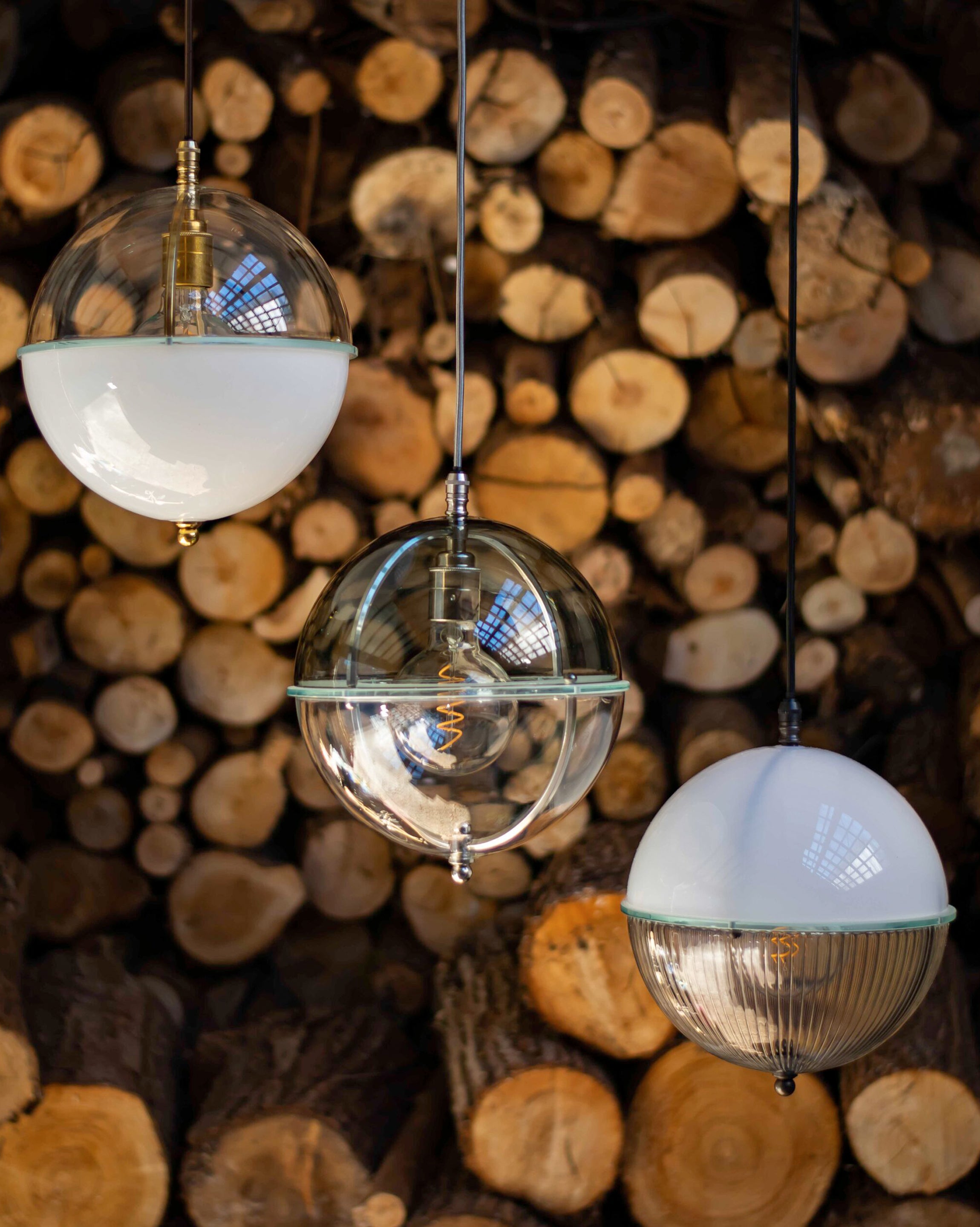 Blue, clear, and white colored glass pendant lights displayed together over stacked natural wood.