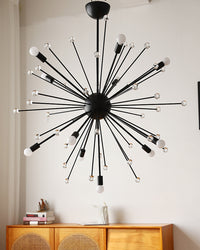 Black living room chandelier installed above a wood cabinet in a neutral interior, showing the sculptural radial frame with the bulbs off.