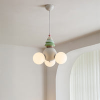 Three-globe globe chandelier suspended near an arched window in a calm neutral room, with a cream body and pastel green tree-like top.