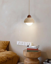 A glass globe pendant light with a travertine dome and walnut cap, casting a soft warm glow above a round bedside table.
