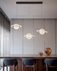 Three planet globes form a linear chandelier above a dark stone counter with upholstered stools in a warm modern interior.