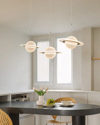 Three glowing planet pendants create a globe chandelier above an oval black dining table in a bright minimalist room.
