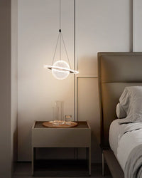 Compact globe pendant with a luminous orbit ring hanging above a bedside table beside a gray upholstered bed.