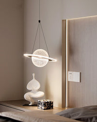 Illuminated LED ring pendant light with a textured planet globe above a bedside ledge with a white sculpture and decorative box.