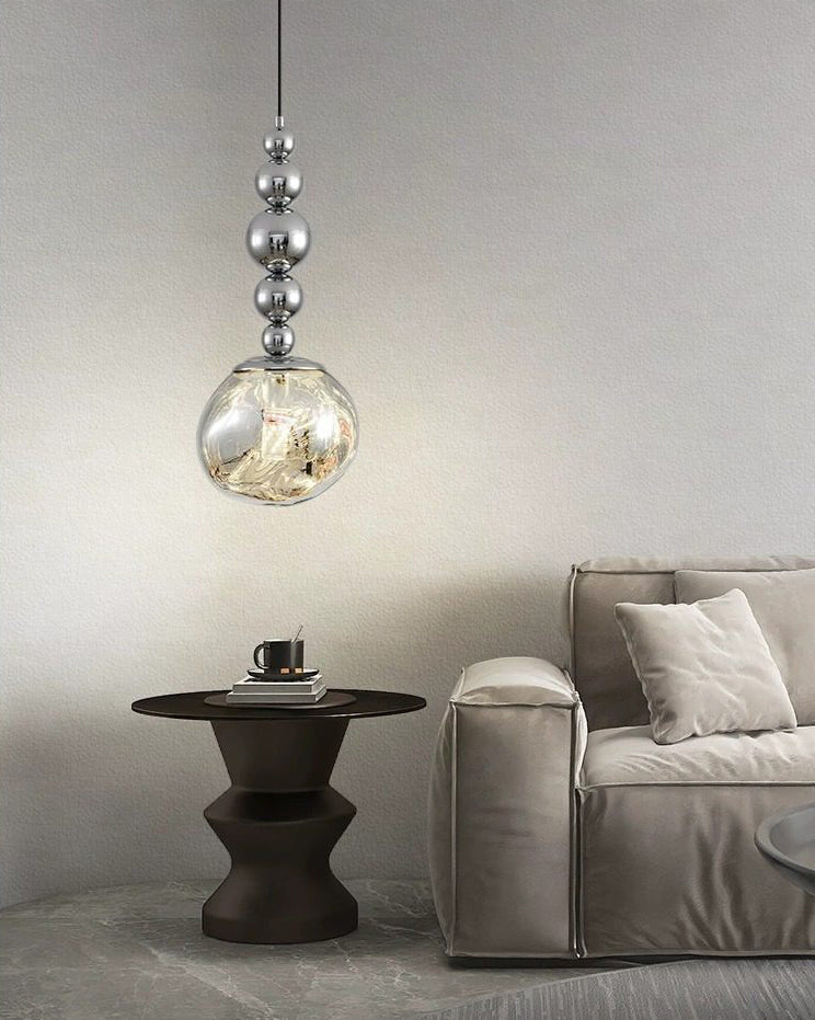 Silver five-sphere minimalist pendant light glowing above a sculptural black side table beside a soft grey sofa.