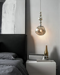 One of the room's hanging bedside lights, a silver five-sphere acrylic globe pendant, glows beside a dark bed above a white nightstand.