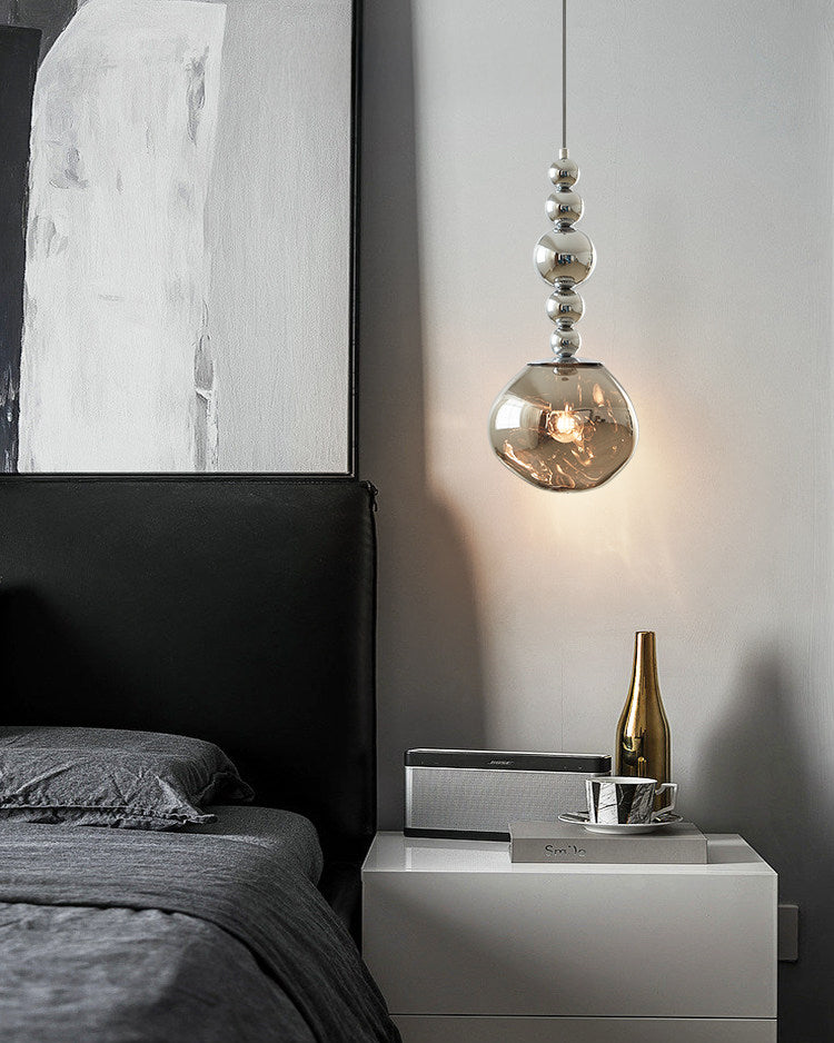One of the room's hanging bedside lights, a silver five-sphere acrylic globe pendant, glows beside a dark bed above a white nightstand.