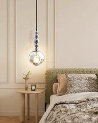 Warm neutral bedroom with a globe light, showing the silver five-sphere pendant lit above a round bedside table beside a green upholstered bed.