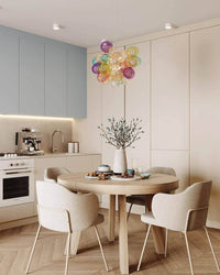 Round dining chandelier with clustered multicolor glass globes centered above a wooden table in a calm modern kitchen and dining space.