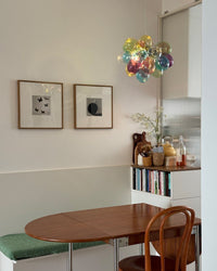 Colorful glass globe chandelier above a compact wooden dining table in a minimalist nook with framed art and ribbed glass.
