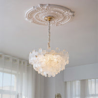 Clear glass flower pendant light with layered petals shown as luminous art deco lighting near sheer curtains.