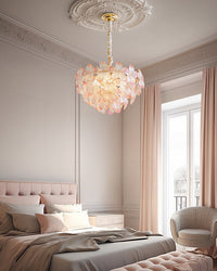 Pink-edged glass flower pendant light glowing above a blush bed beneath an ornate white ceiling medallion.