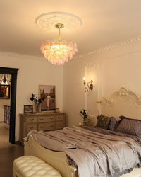 Layered glass flower pendant light casting warm light over a cream bedroom with a full-length mirror and sheer curtains.