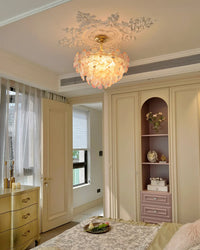 Pink glass flower pendant light creating warm vintage lighting above an ornate bed with a dresser and wall sconce.