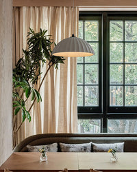Fluted plaster pendant centered over a dining nook with a built-in bench, greenery, and black-framed windows, creating calm dining room lighting.