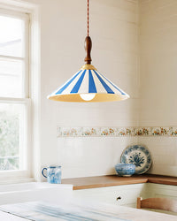 Blue-striped ceramic pendant lamp with an exposed bulb above a kitchen dining corner with white tile, wood counters and blue tableware.