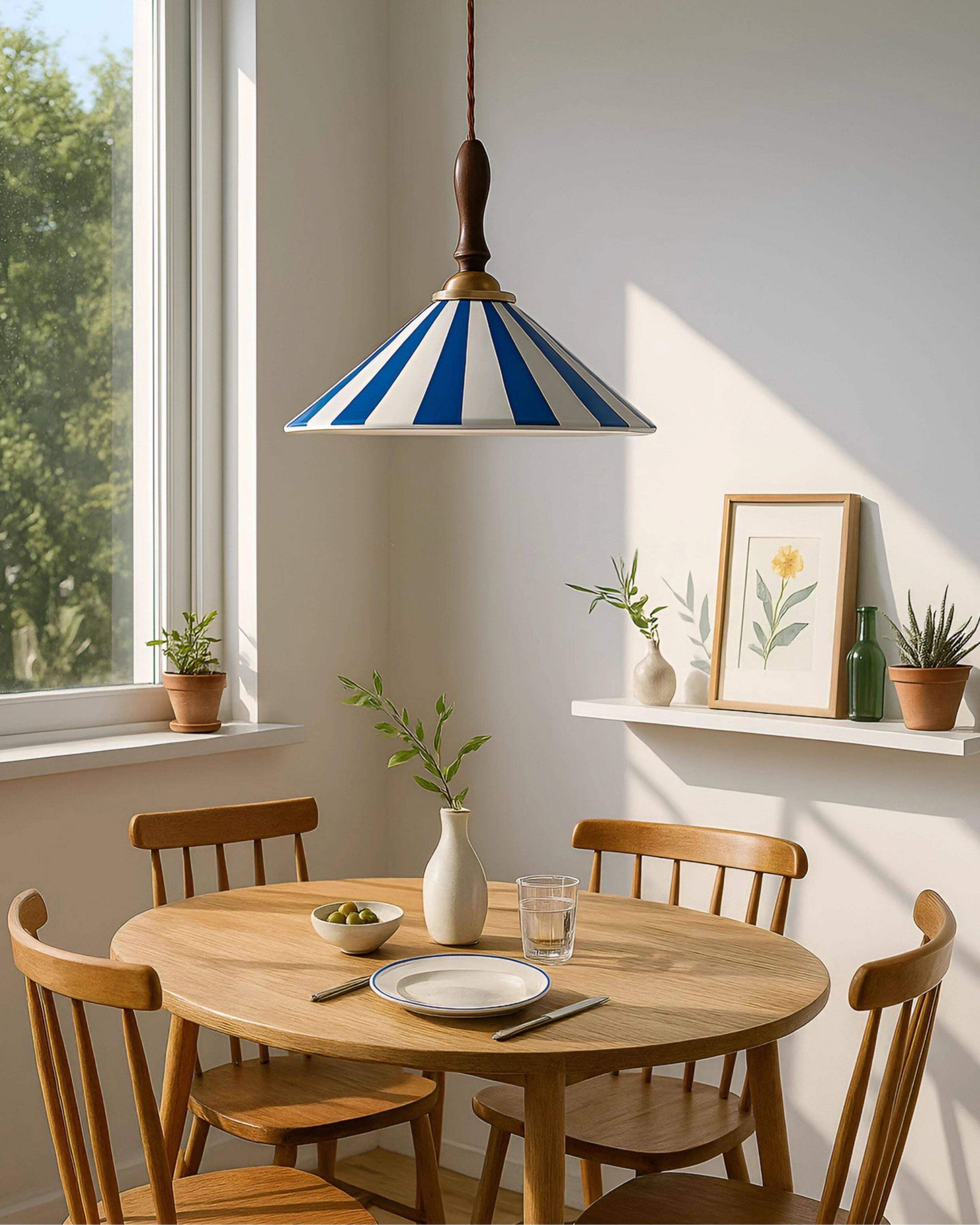 Blue-striped vintage ceramic pendant light centered above a round wooden dining table in a bright room with plants and framed floral art.