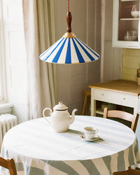 Blue-striped ceramic pendant light above a round breakfast table set with a white teapot in a softly lit vintage-style kitchen.