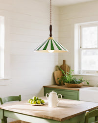 Green-striped ceramic pendant light hanging above a wood kitchen table in a white cottage-style room with green cabinetry and a bowl of apples.