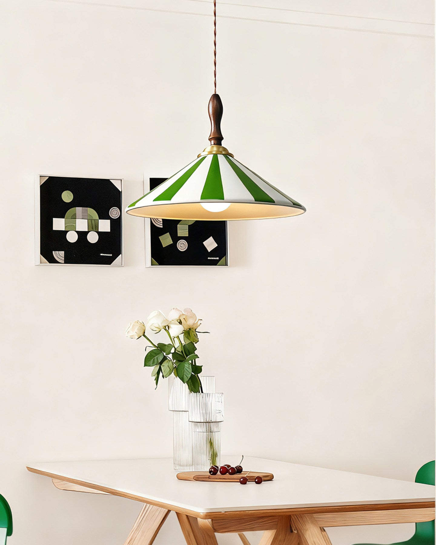 Green pendant light with white ceramic stripes and a dark wood handle above a rectangular dining table with clear vases, flowers and abstract wall art.