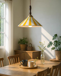 Yellow-and-white dining light fixture above a wooden table in a sunlit room with plants, coffee cups and warm natural finishes.