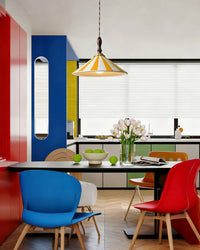 Yellow-striped ceramic pendant light above a black dining table in a bold red, blue and green kitchen with colorful molded chairs.